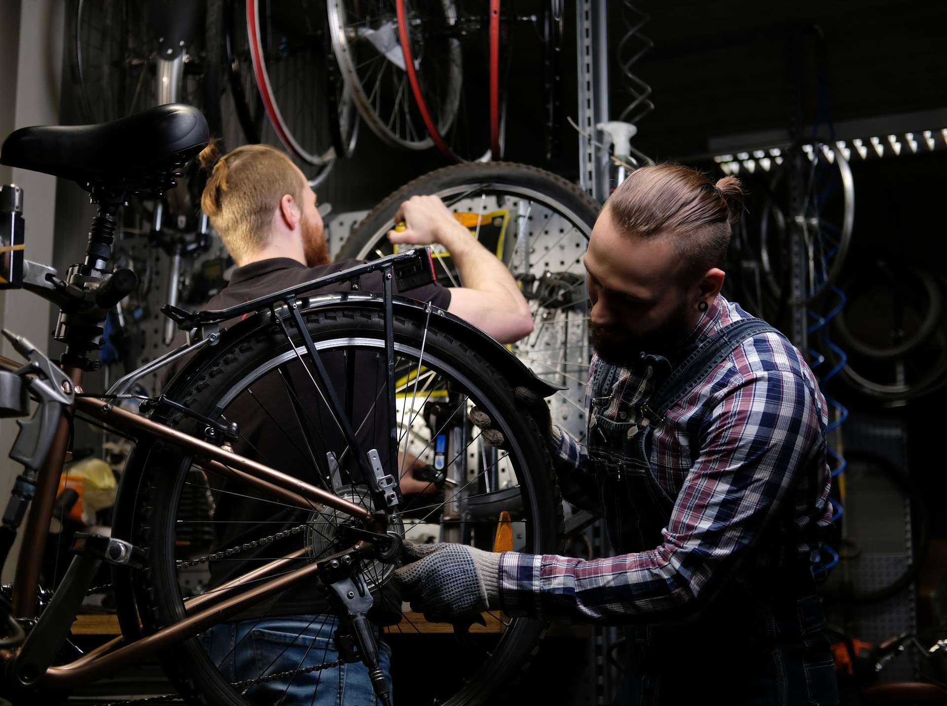 Two handsome stylish male working with a bicycle in a repair shop. Workers repair and mounts bike in a workshop