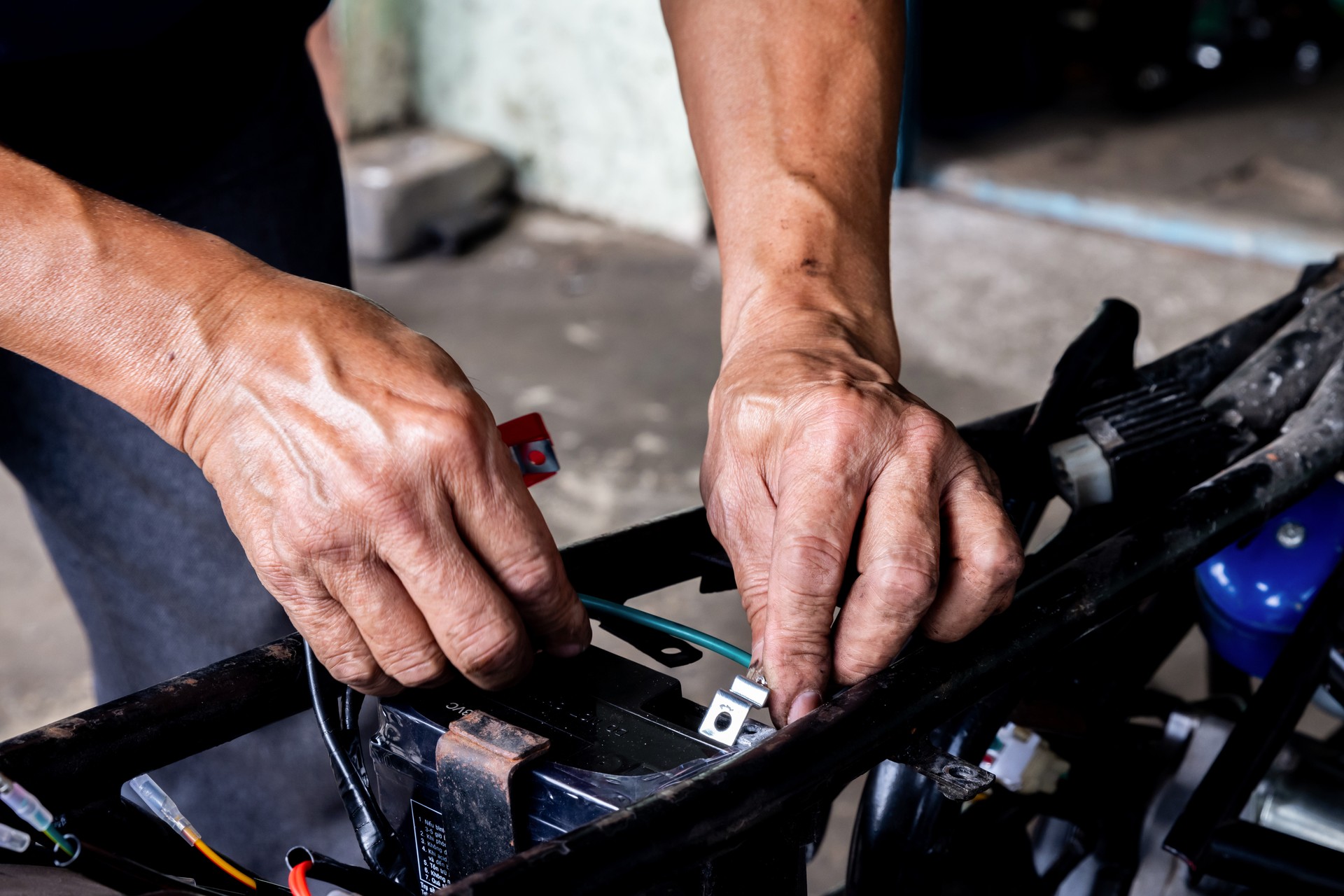 Close up photo on the hands of a man connecting the cables to the battery of a motorcycle.